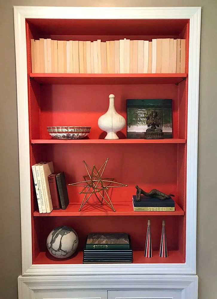 A red bookshelf with white trim displays books, decorative objects, and art pieces arranged on four shelves.