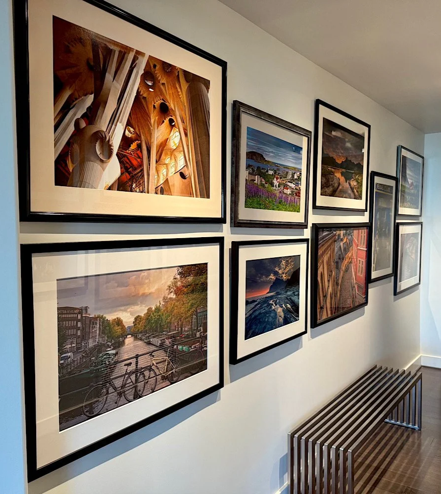 Wall with framed photographs of cityscapes, landscapes, and architecture in a gallery or museum setting.