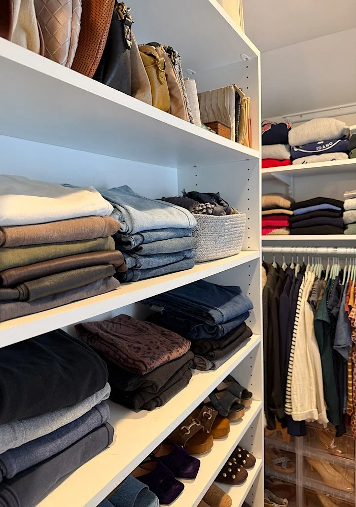 Closet with shelves of folded clothes, handbags on the top shelf, and hanging clothes on the right.