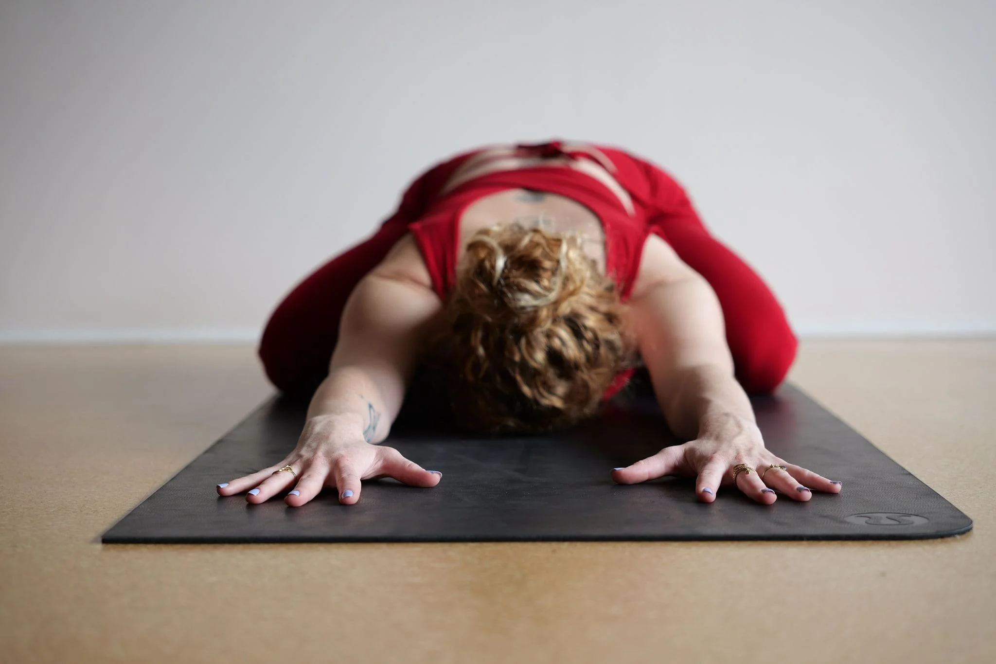 Une personne pratiquant le yoga en position de chien tête en bas sur un tapis noir, dans une pièce lumineuse.