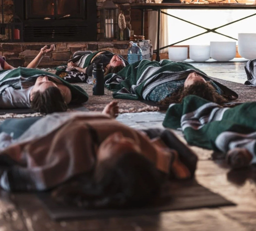 Groupe de personnes allongées et médite dans une pièce calme avec cheminée et grandes coupes blanches en arrière-plan.