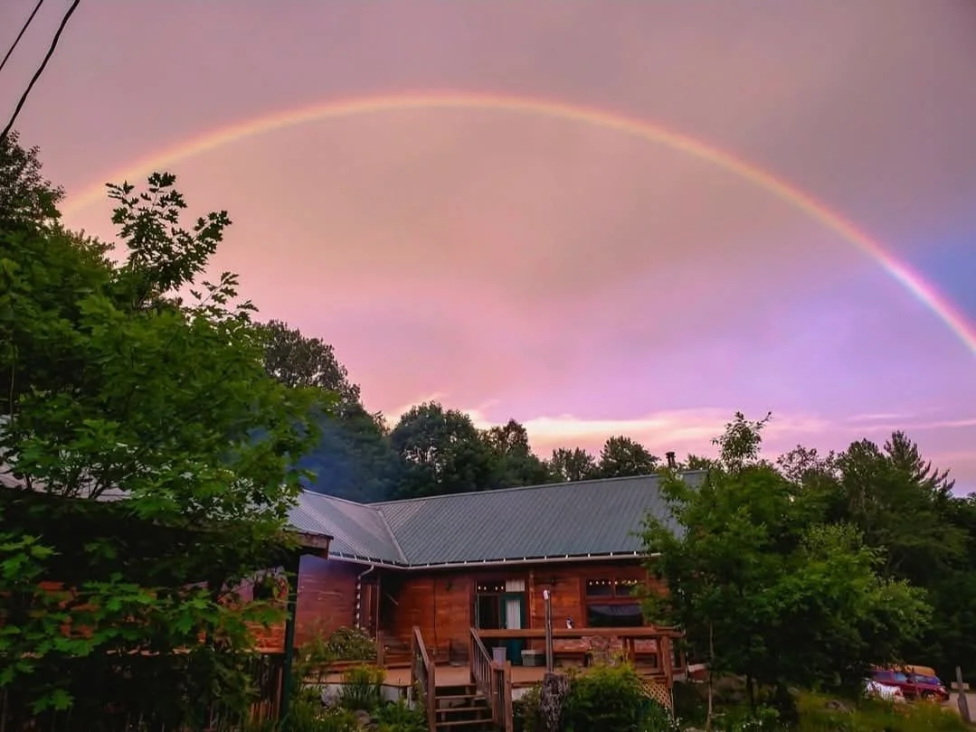 Arc-en-ciel au-dessus d'une maison en bois avec un ciel coloré au crépuscule.