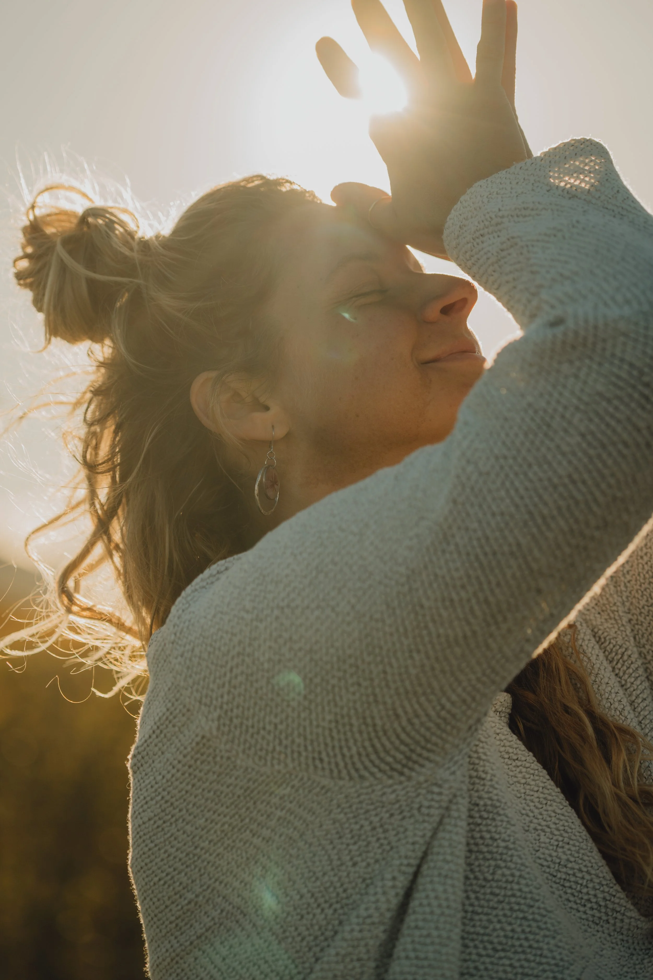 Jeune femme souriant faisant face au soleil, dans un champ, qui fait un mudra de yoga.
