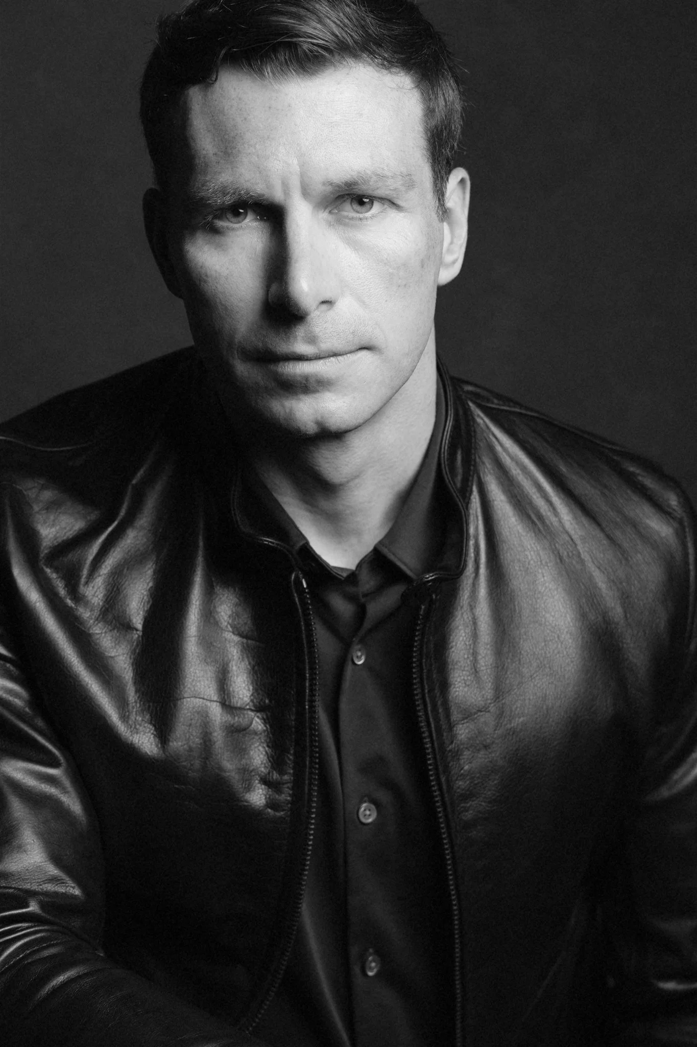 Black and white portrait of composer Ryan Stauffer wearing a leather jacket.