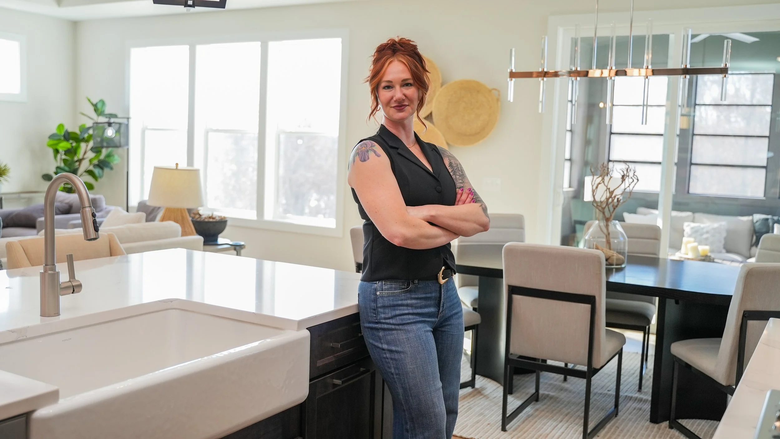 Realtor standing in modern, bright kitchen and dining area with arms crossed, smiling at camera.