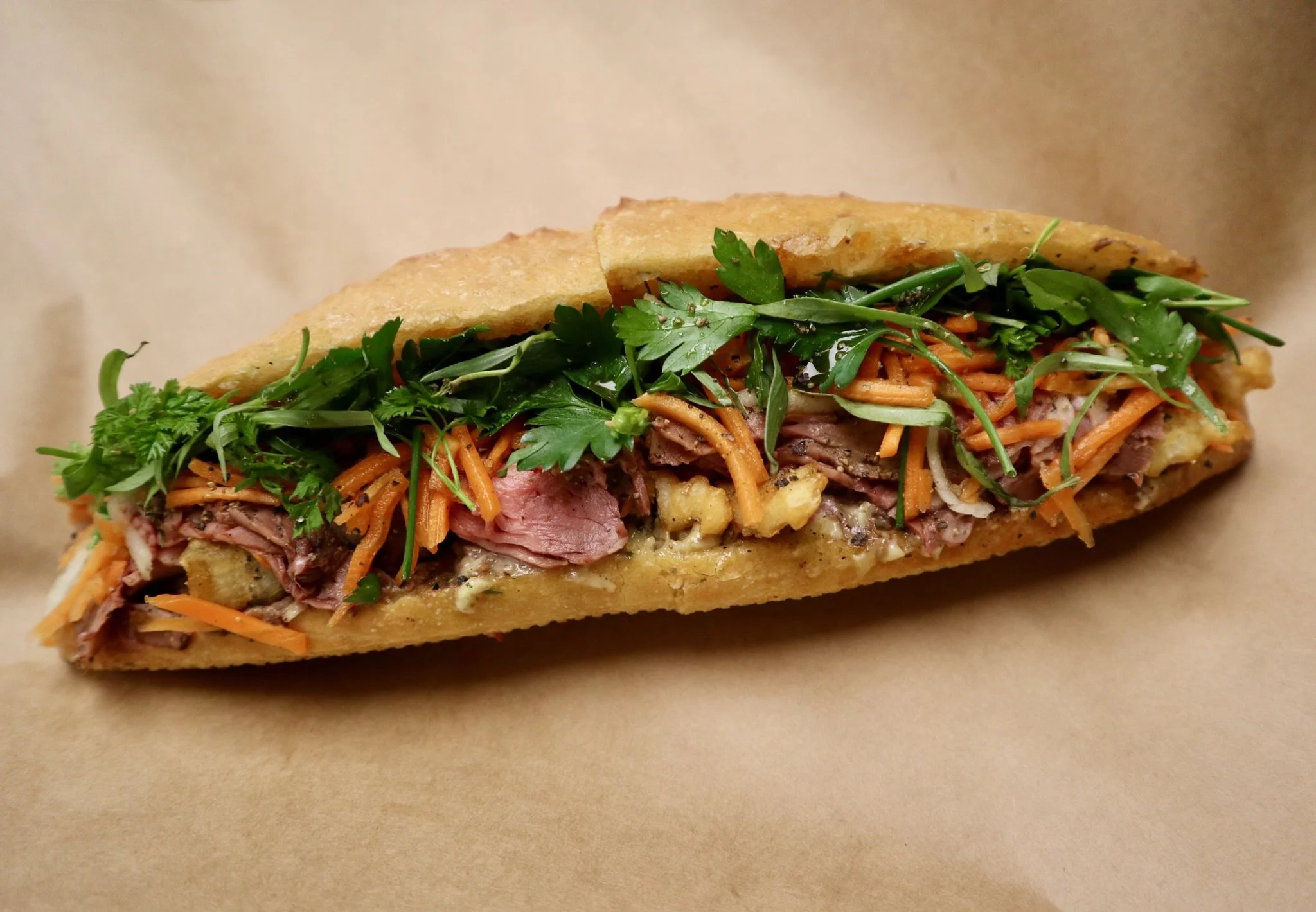 Philly cheesesteak sandwich with chopped steak, shredded cheese, and fresh herbs in a hoagie roll on brown paper