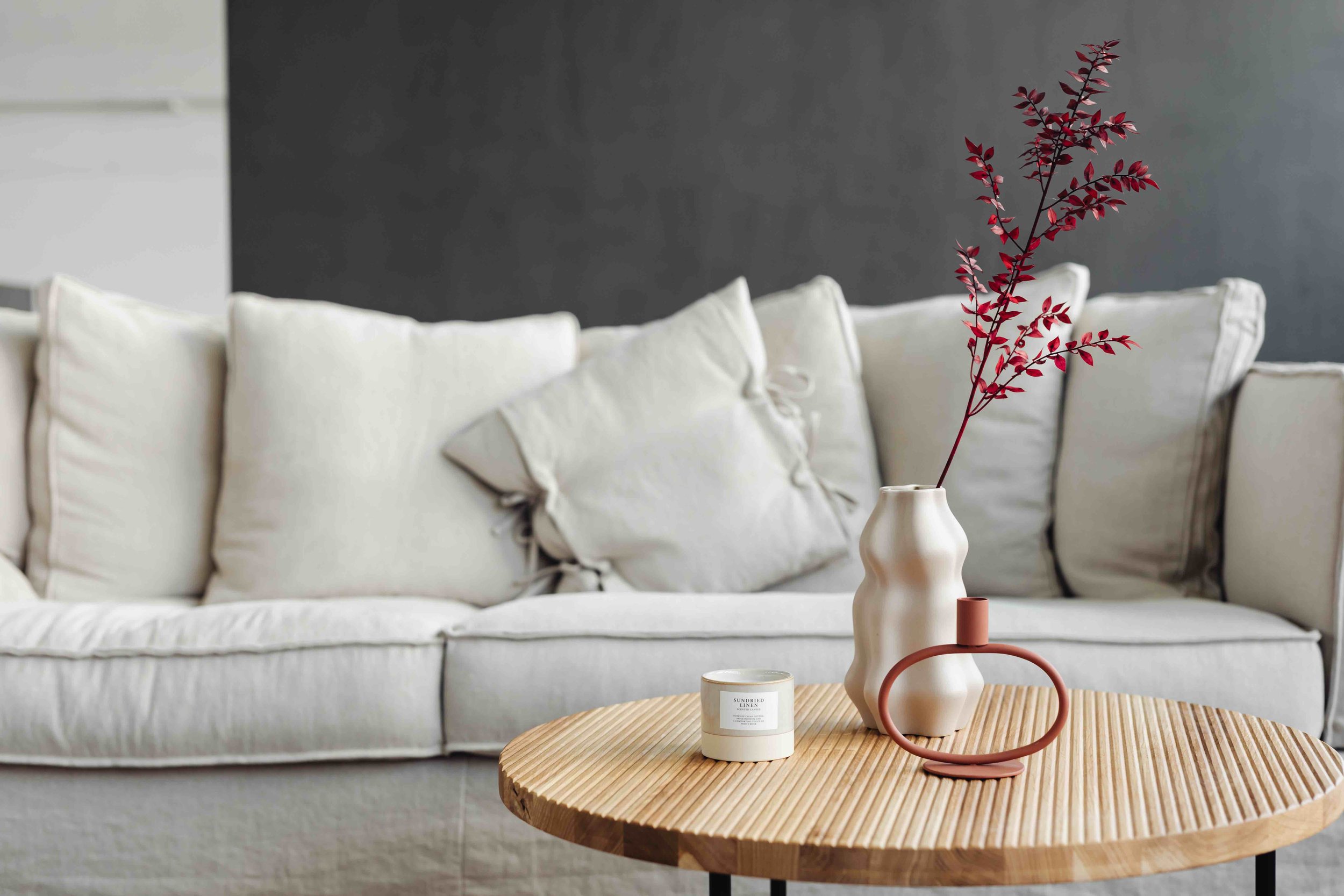 Light grey couch and wood coffee table with candle and vase with stem of red leaves in it