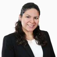 Headshot of a woman with dark hair wearing a black blazer and white top, smiling against a plain white background.