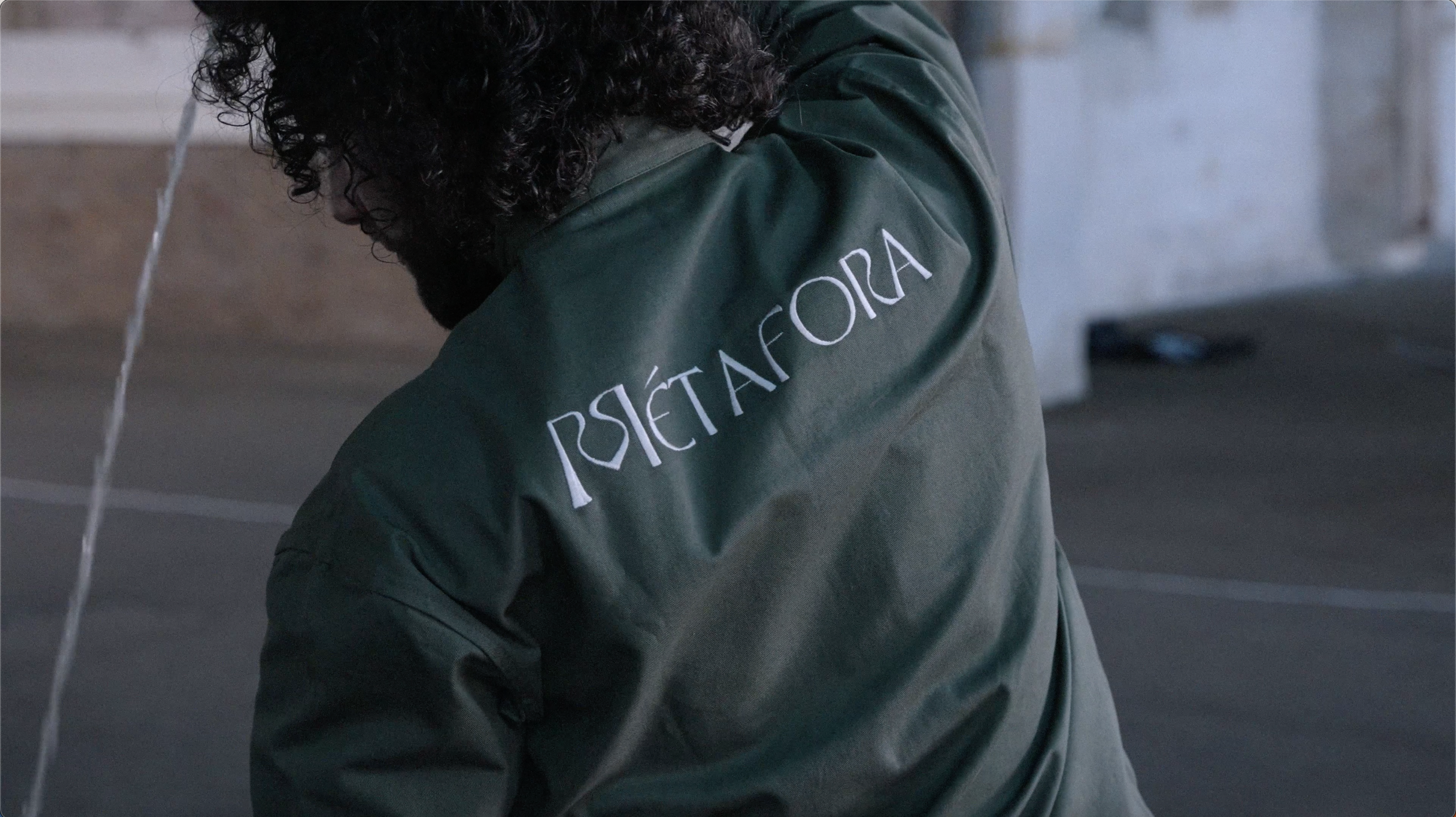 A person with curly dark hair wearing a green jacket with the word 'RESIDENTA' written on the back in white letters.