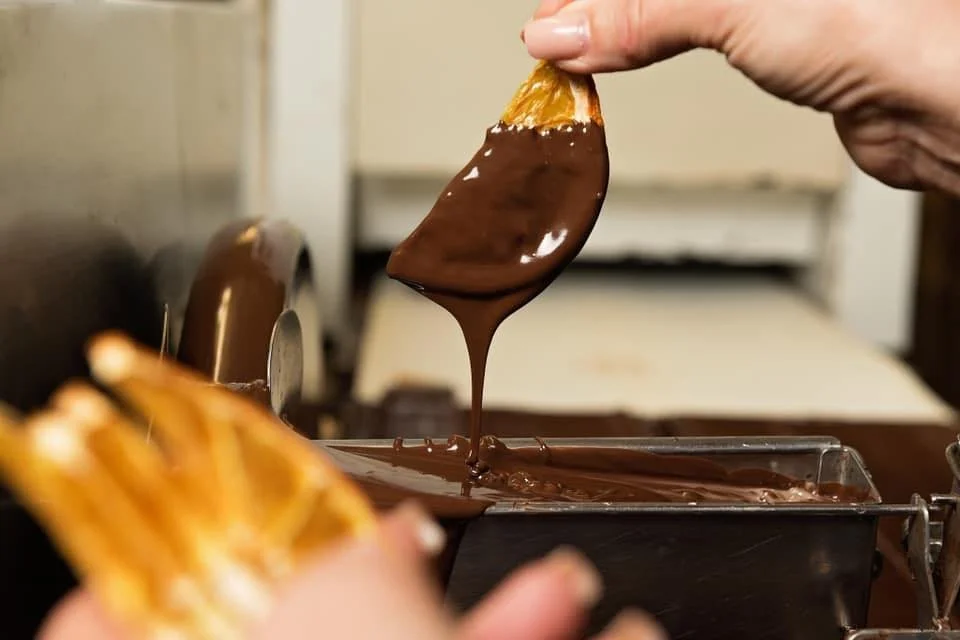 A hand dipping a dried orange slice into melted chocolate.
