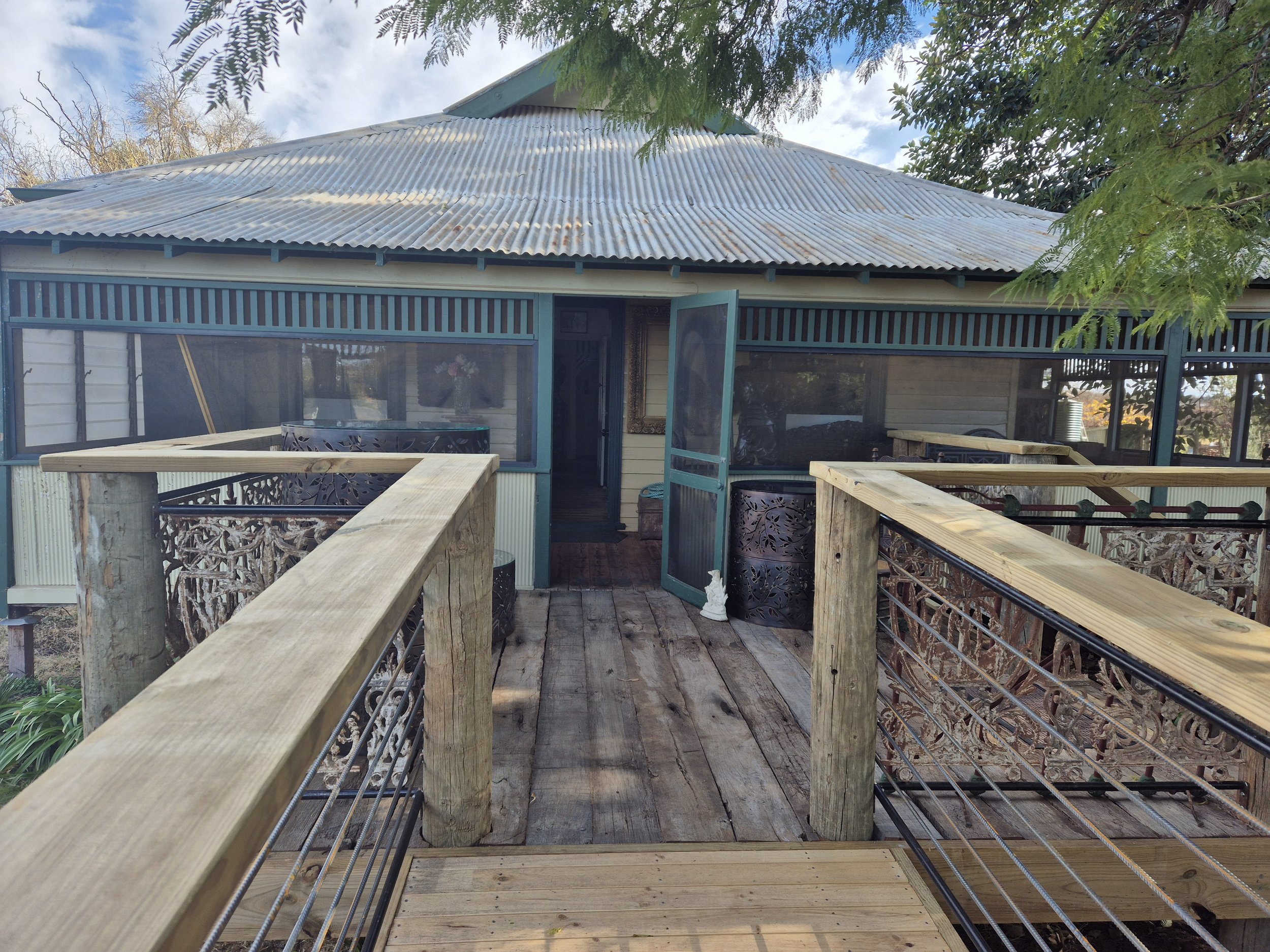 A wooden deck leading to Roy Farms Storefront, with a tin roof, screened porch, open door, and decorative metal railing.
