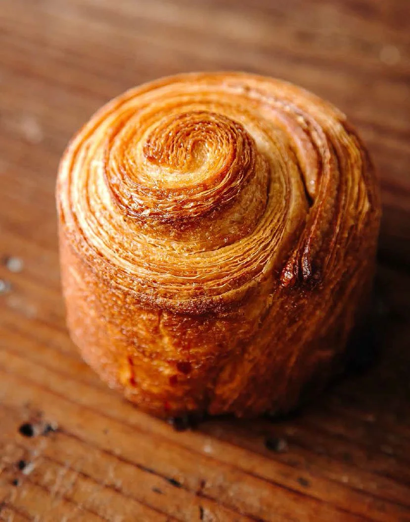 A close-up of a hand-crafted freshly baked flake pastry on a rustic wooden board.