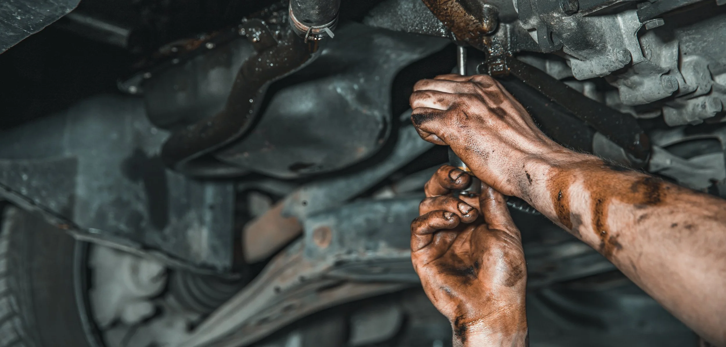 Mechanic's dirty hands working underneath a car, fixing or inspecting the car's underside.