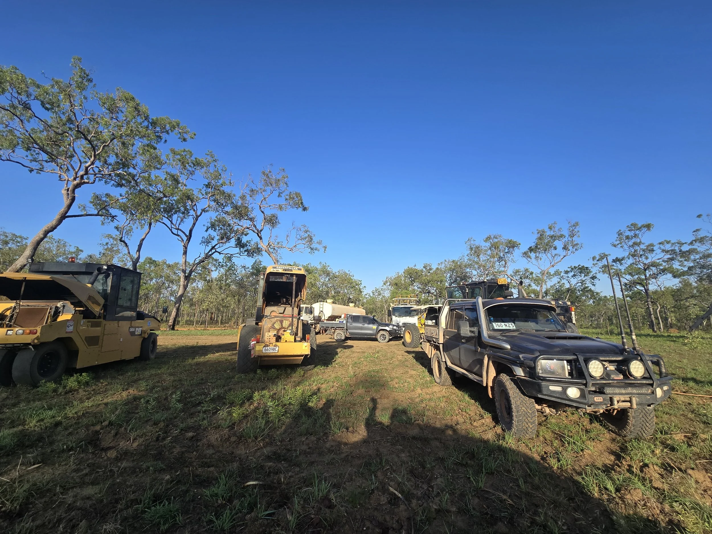 Off-road vehicles parked on grassy land under a blue sky with scattered trees.