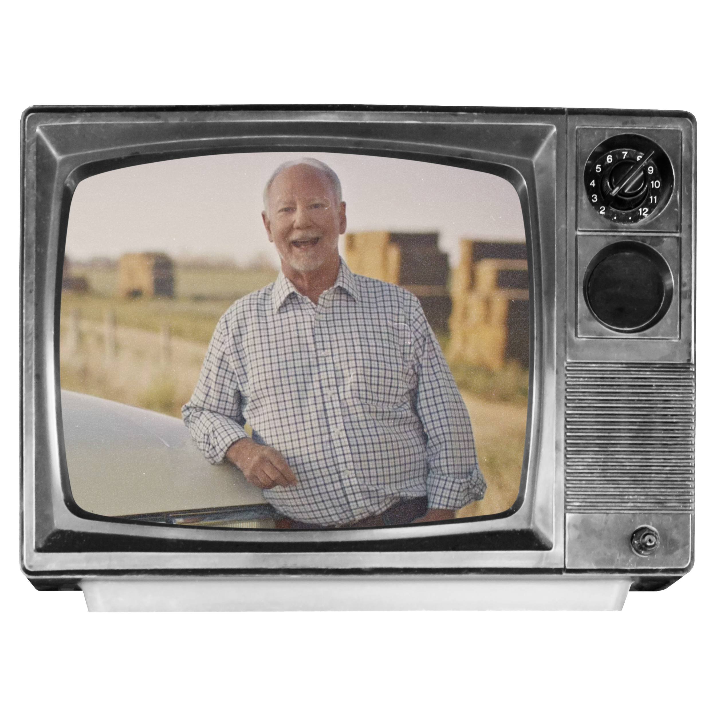 A man in a checkered shirt standing outdoors in front of a field with hay bales, viewed through the screen of an old black-and-white television.