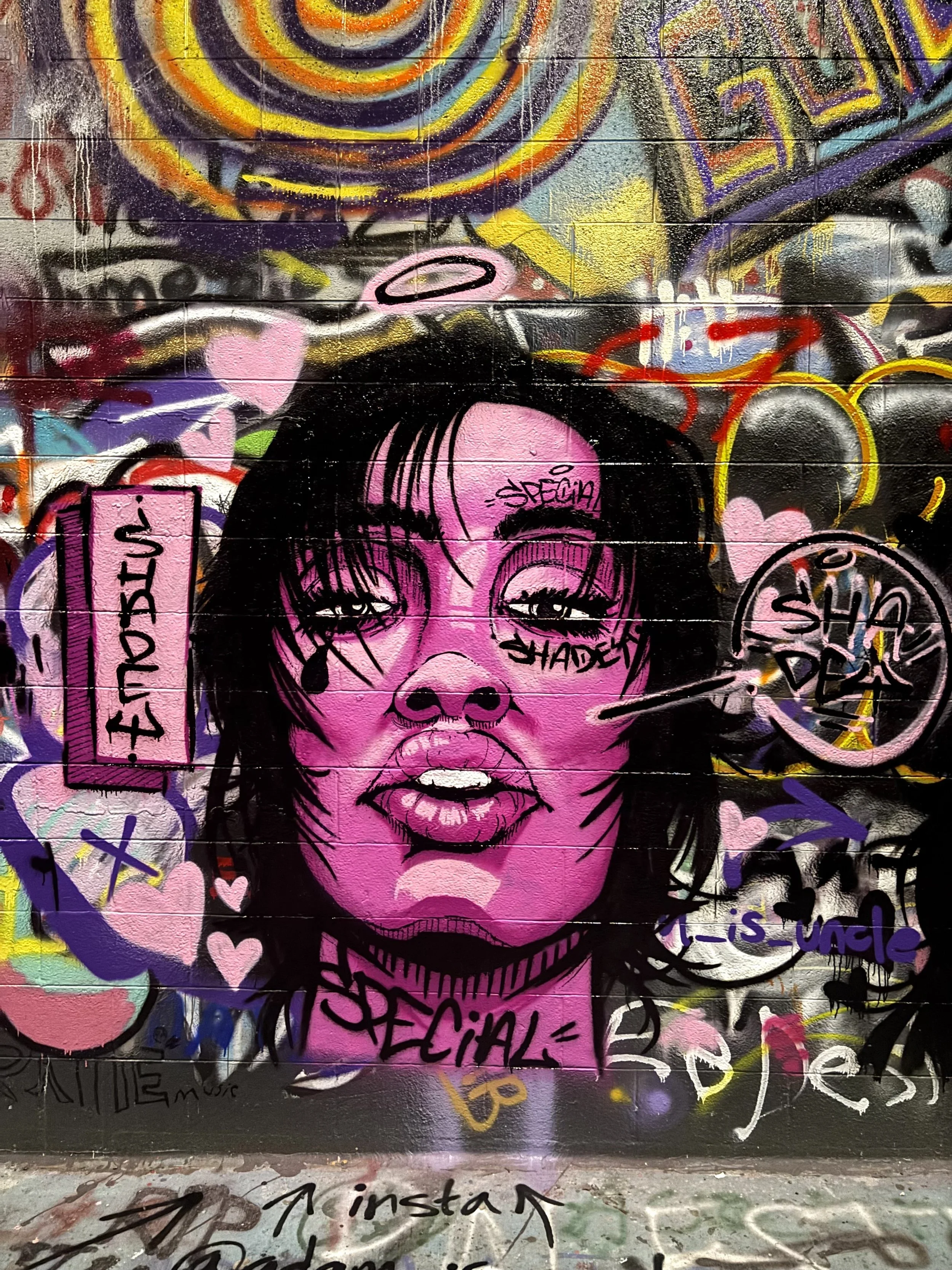 Graffiti mural of a woman with pink skin and black hair, with the words 'special,' 'shadow,' and 'sh! dea' and various abstract and colorful elements surrounding her.