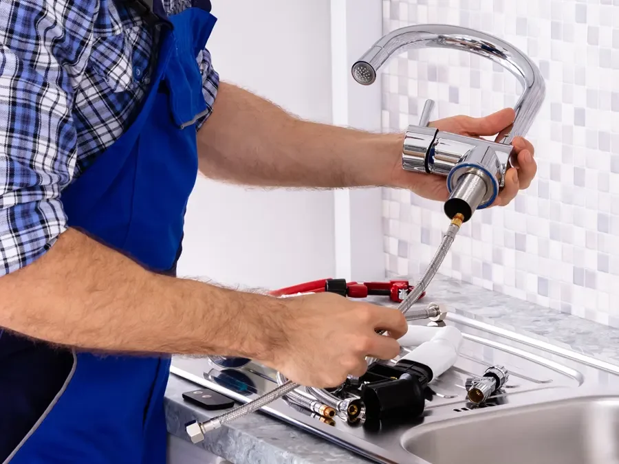 A person in a blue apron installing a kitchen faucet.