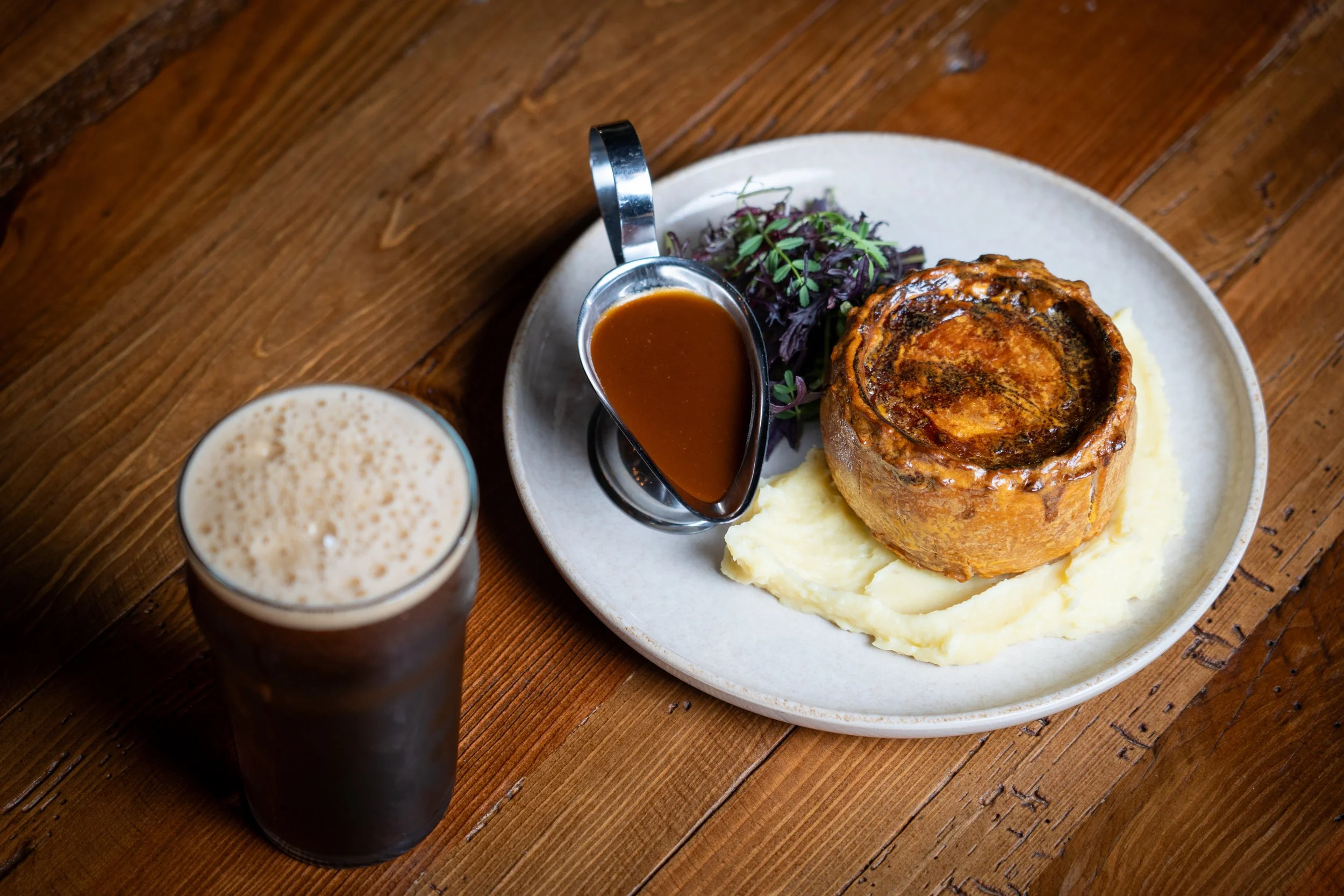 Meat pie with gravy and mash on a plate beside a pint of beer.