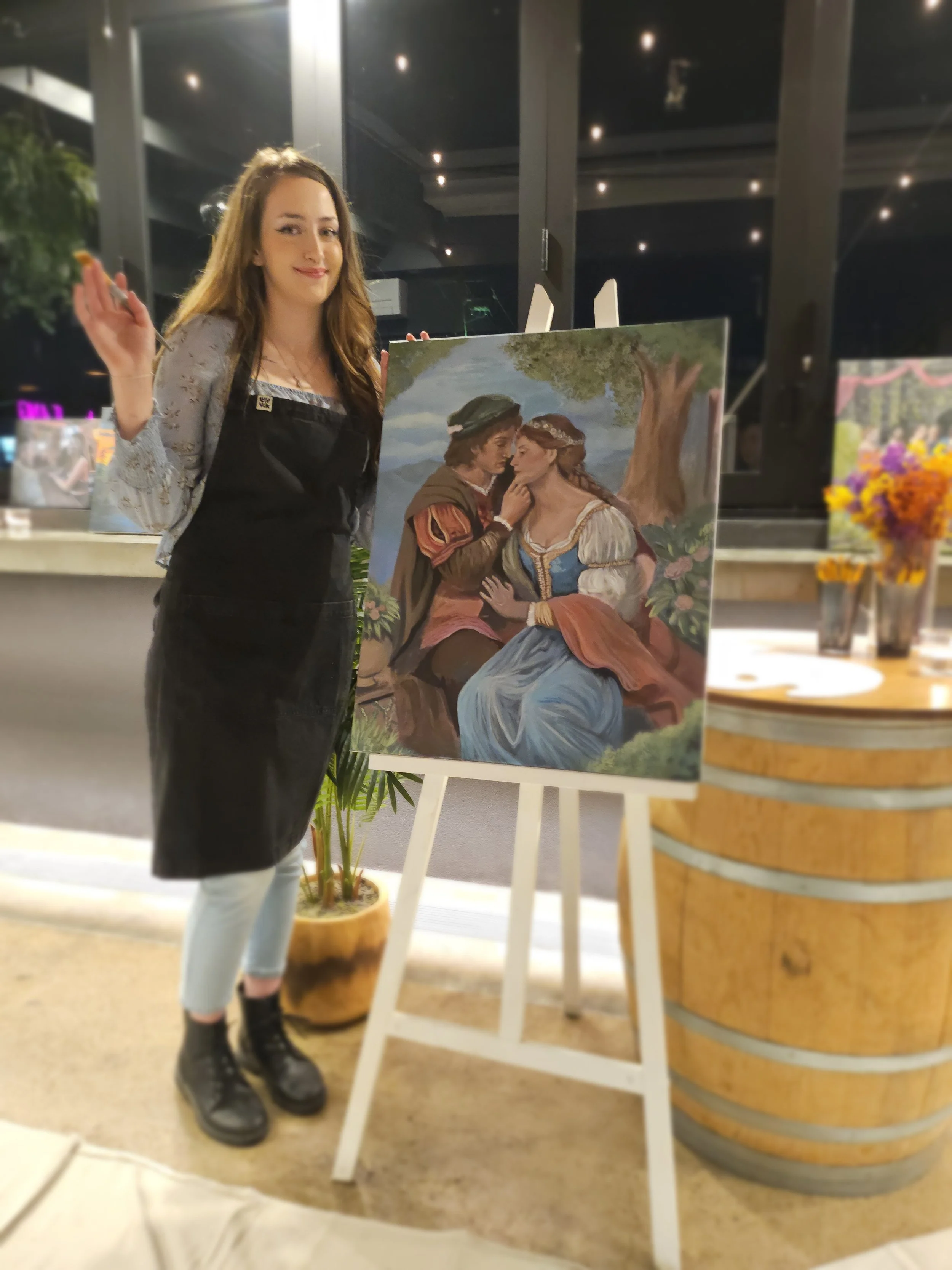 Women next to easel with painting and a paintbrush.