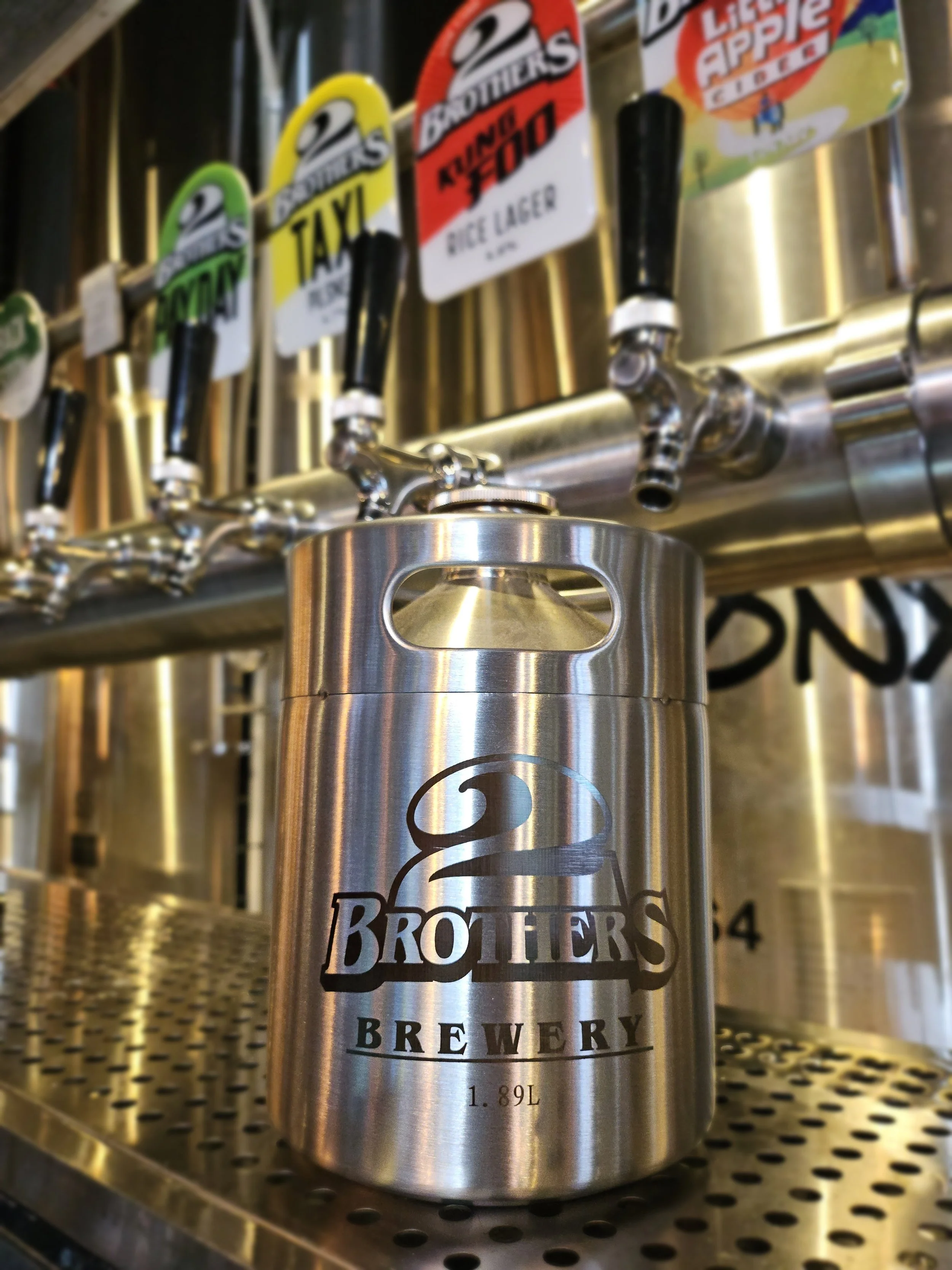 Close-up of a stainless steel beer tap handle with the logo of Brothers Brewery, showing the volume of 1.89 liters, on a metal beer tap system.