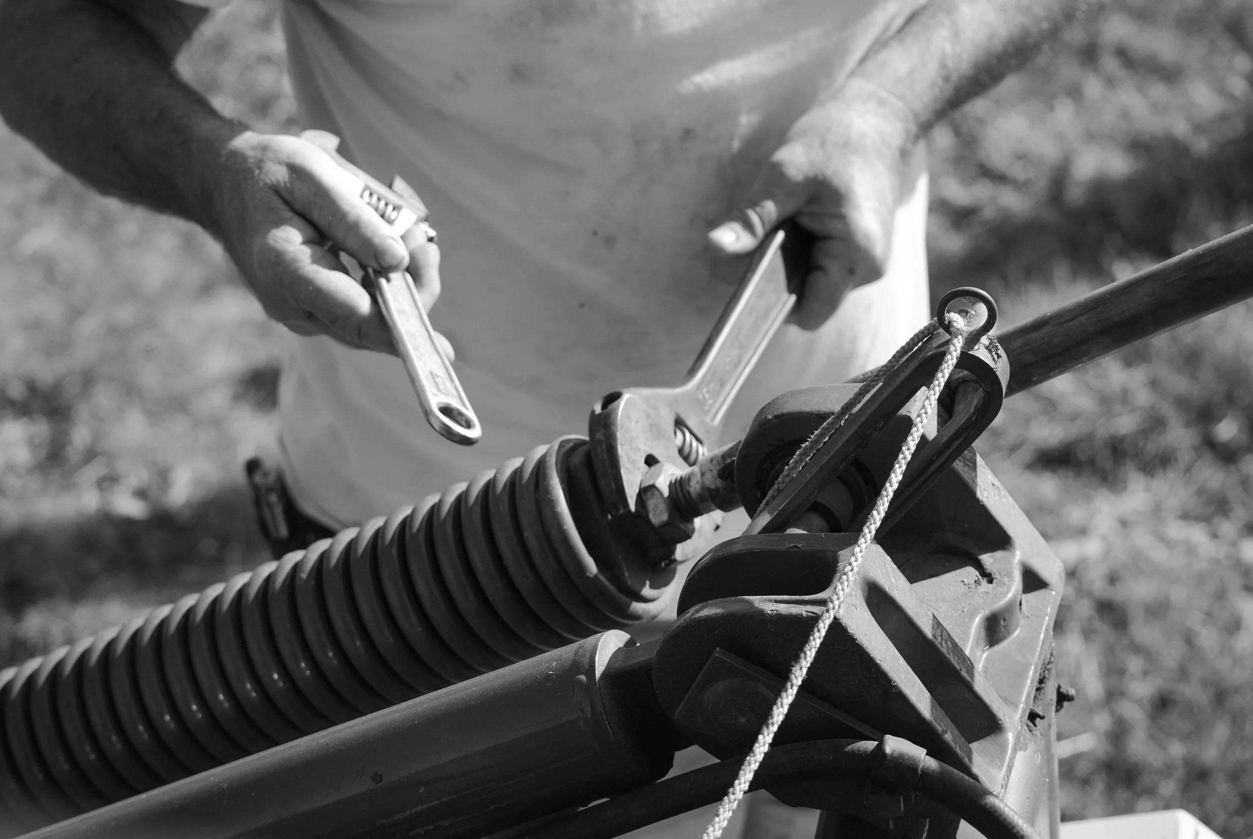 Close-up of a person using a wrench to work on machinery, with hands and machinery parts visible in black and white.