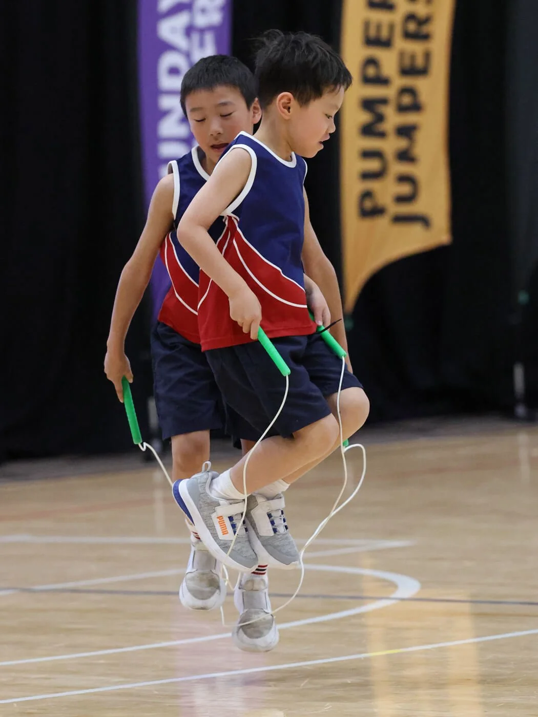 Two young boys jumping rope together in a gymnasium.