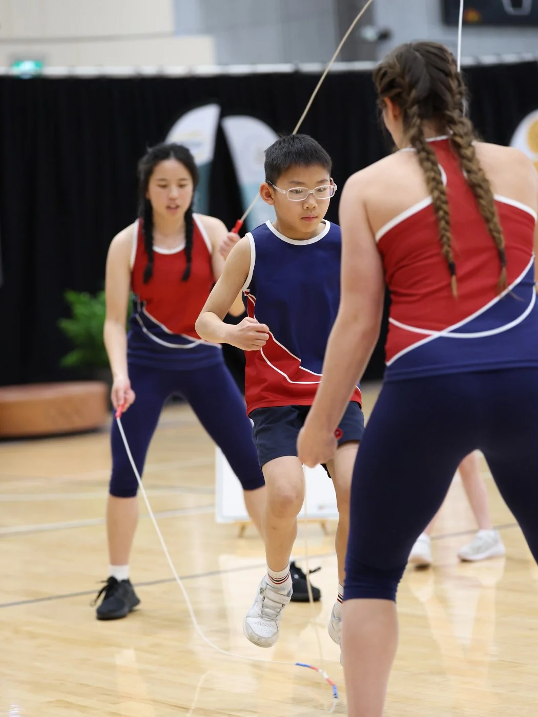 Kids playing jump rope indoors, wearing sports uniforms.