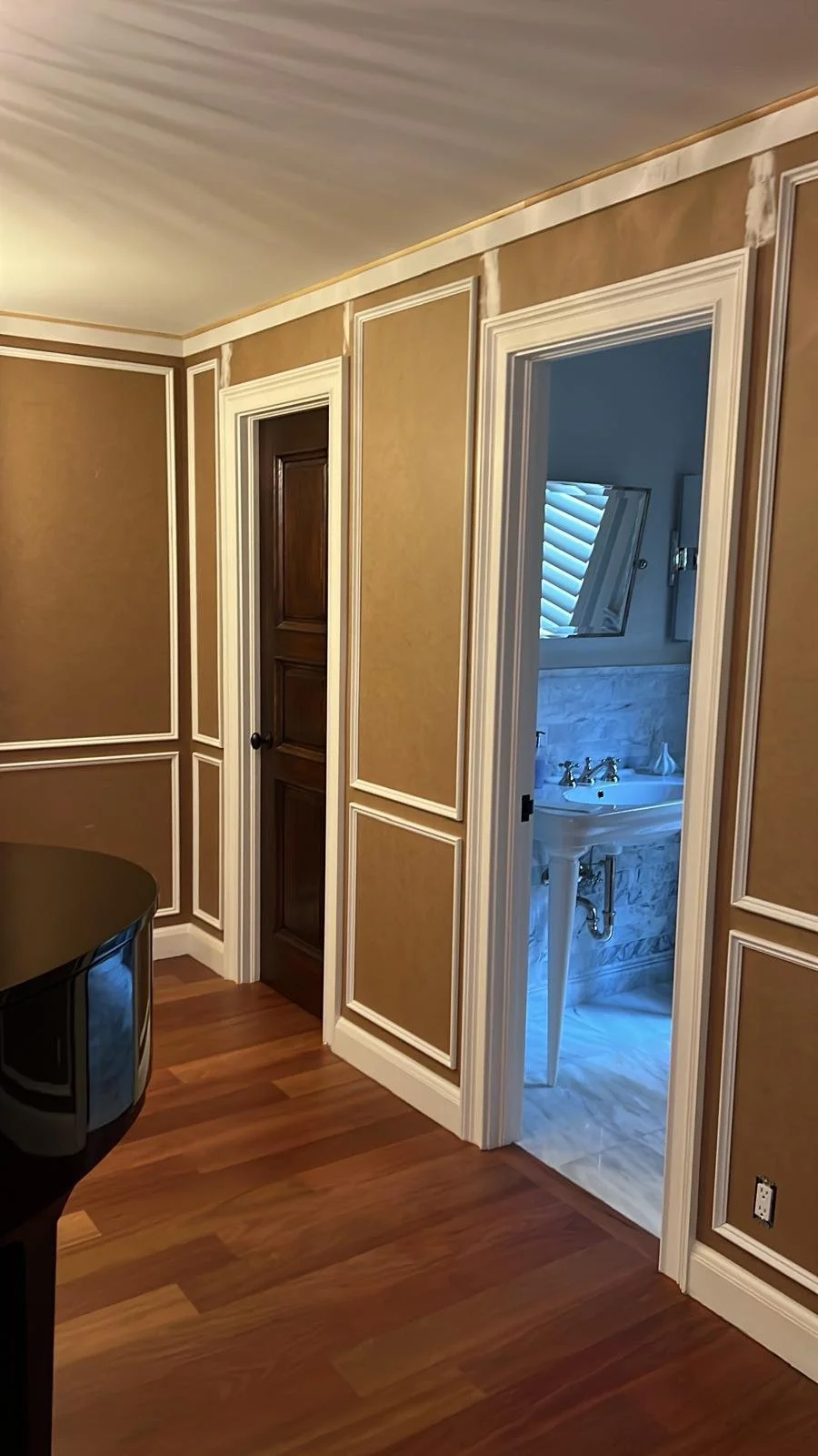 View of an interior room with a small doorway leading to a bathroom with a pedestal sink, marble walls, and a slanted window.