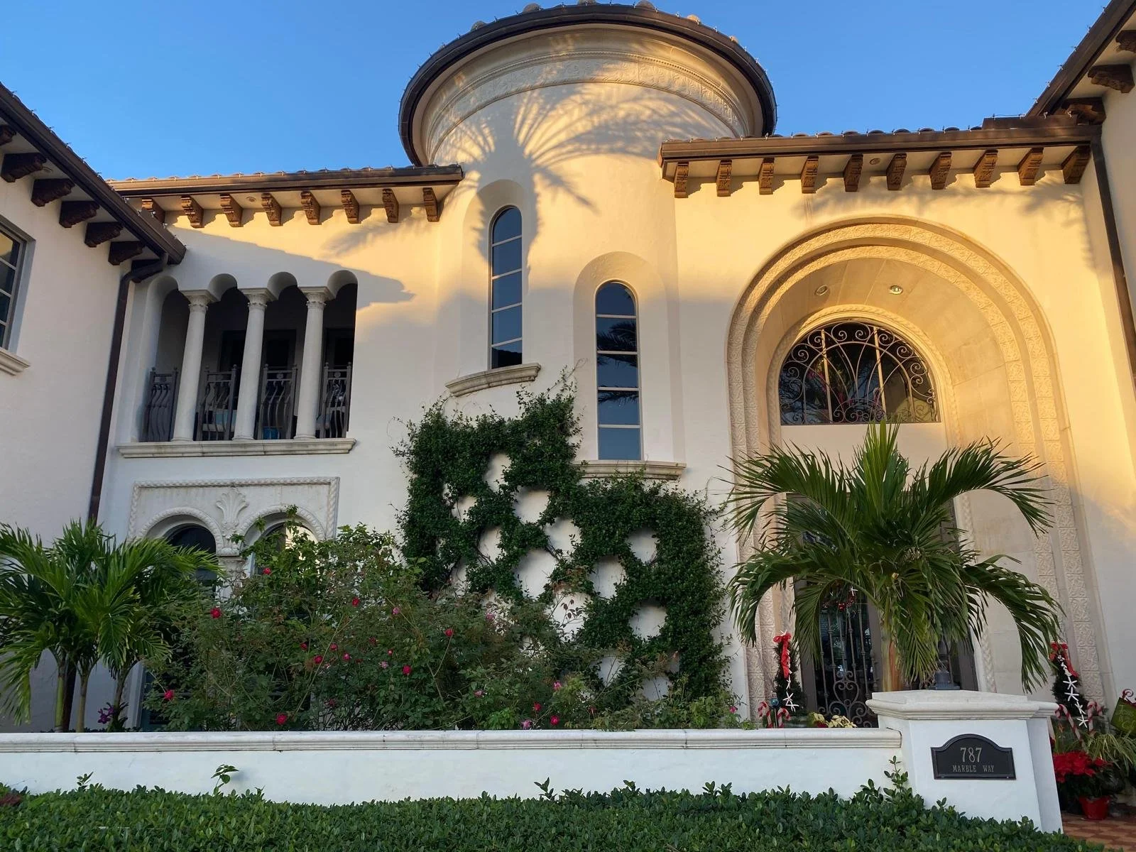 Elegant Mediterranean-style house with arched windows, balconies, and lush landscaping illuminated by warm sunset light.