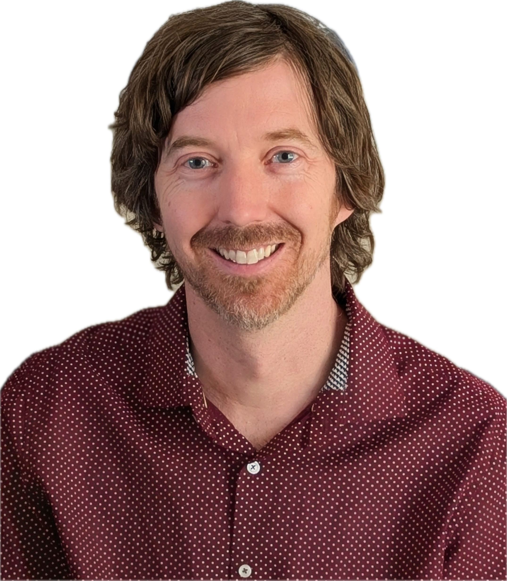 Close-up of a smiling man with light skin, light brown curly hair, and a short beard, wearing a maroon shirt with white polka dots.