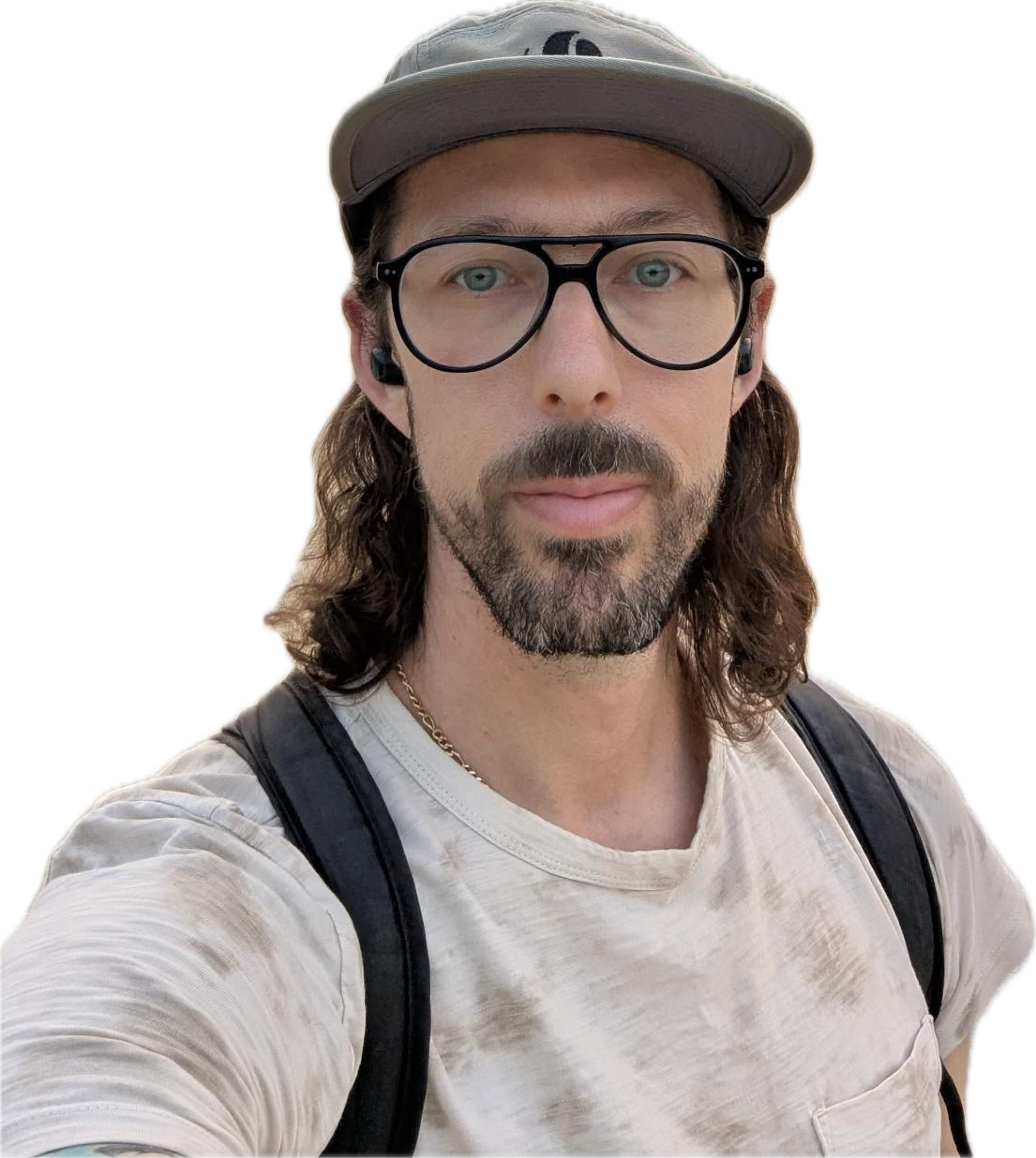 A man with long brown hair, glasses, and a beard wearing a beige t-shirt, a gray cap, and a black backpack.