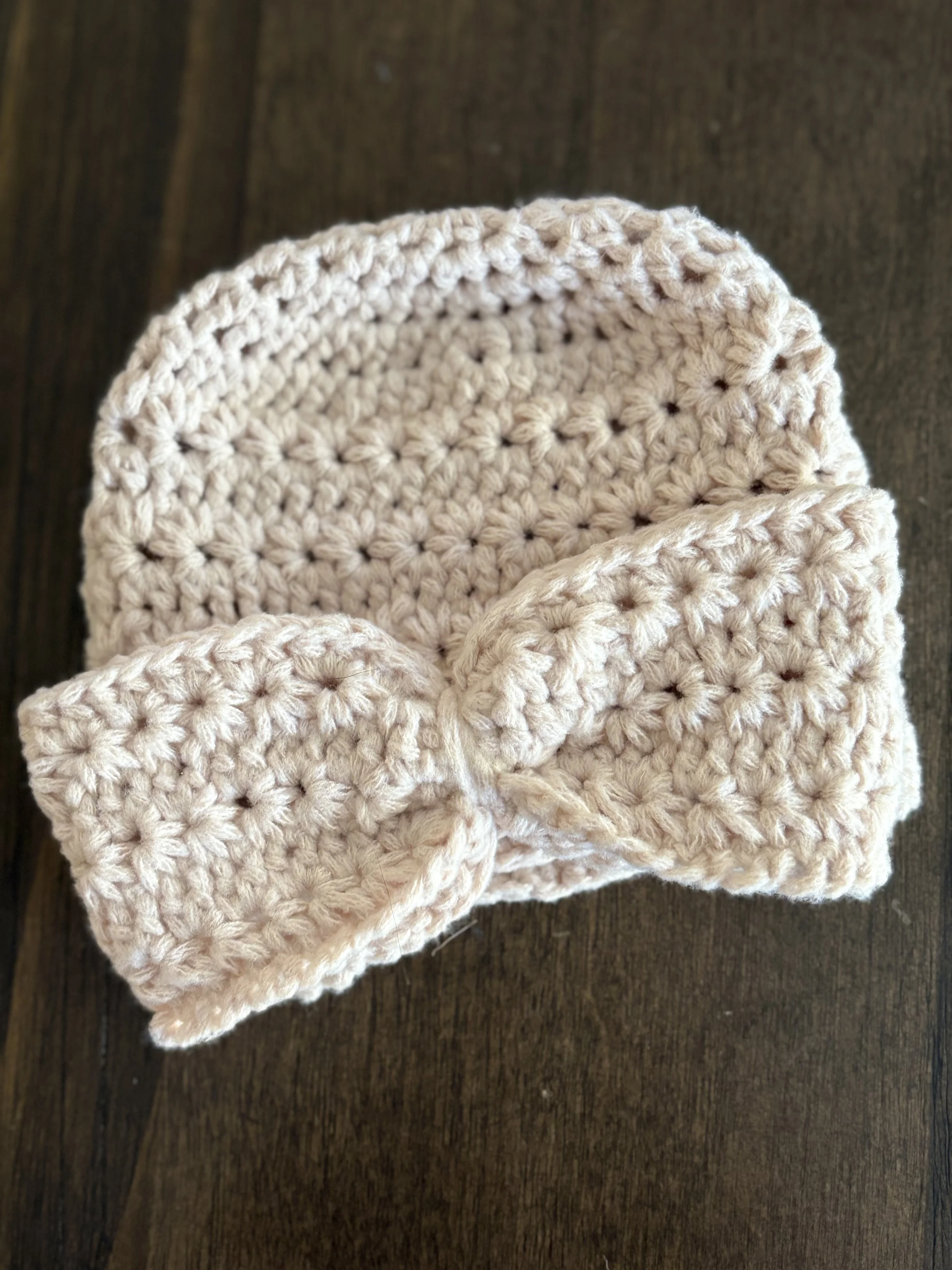 Cream crocheted headband with bow on dark wood surface