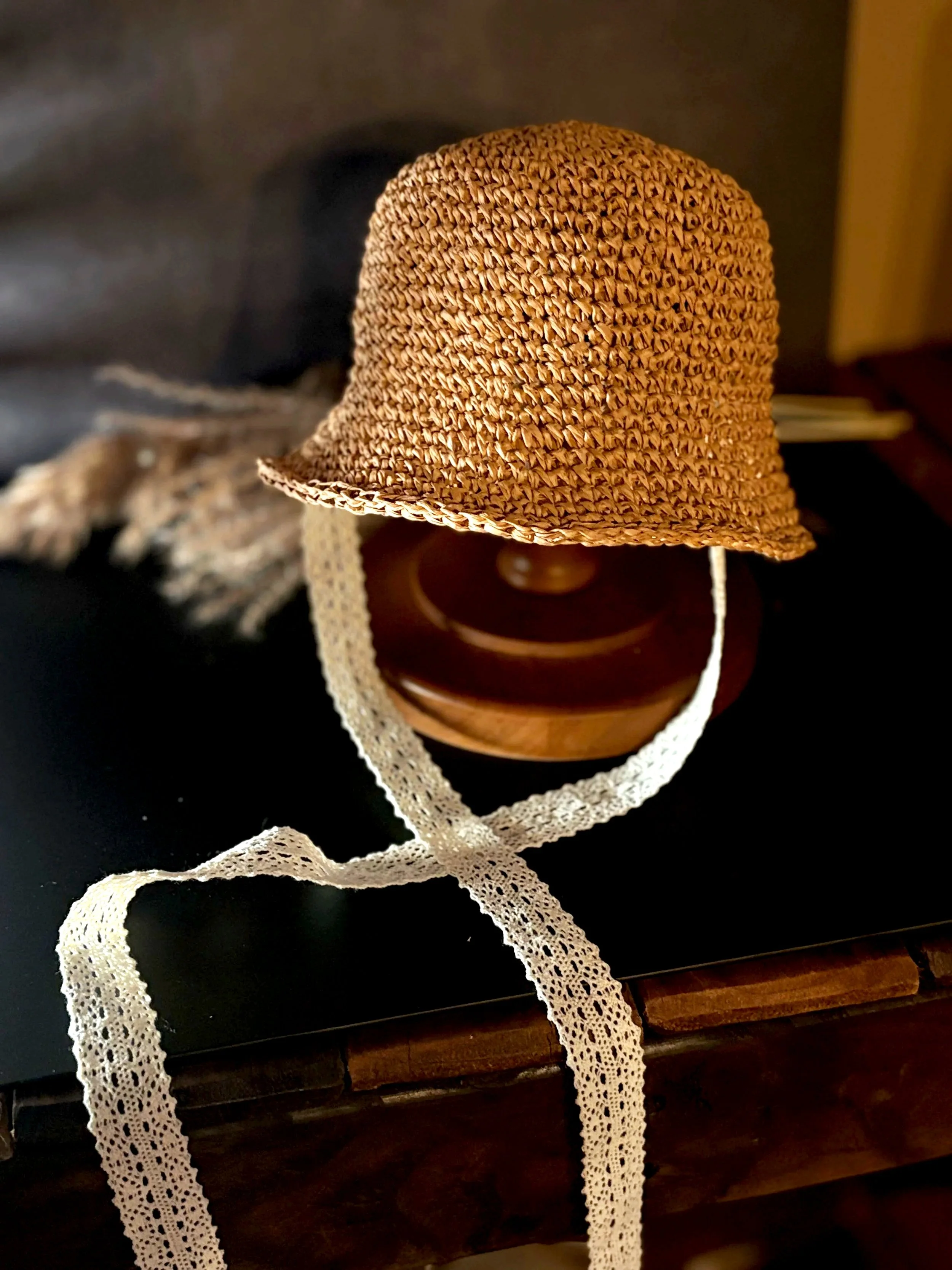A woven straw hat with a wide brim resting on a wooden surface, with a lace ribbon trailing from it.