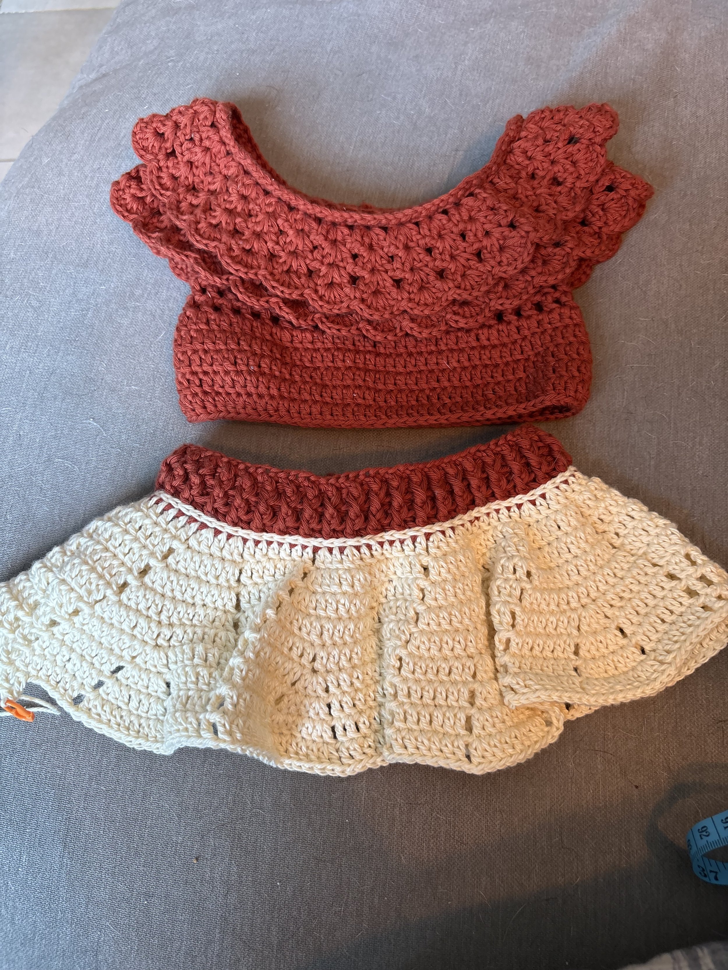 Close-up of handcrafted crochet skirt and crop top outfit,  laid on a gray fabric surface.