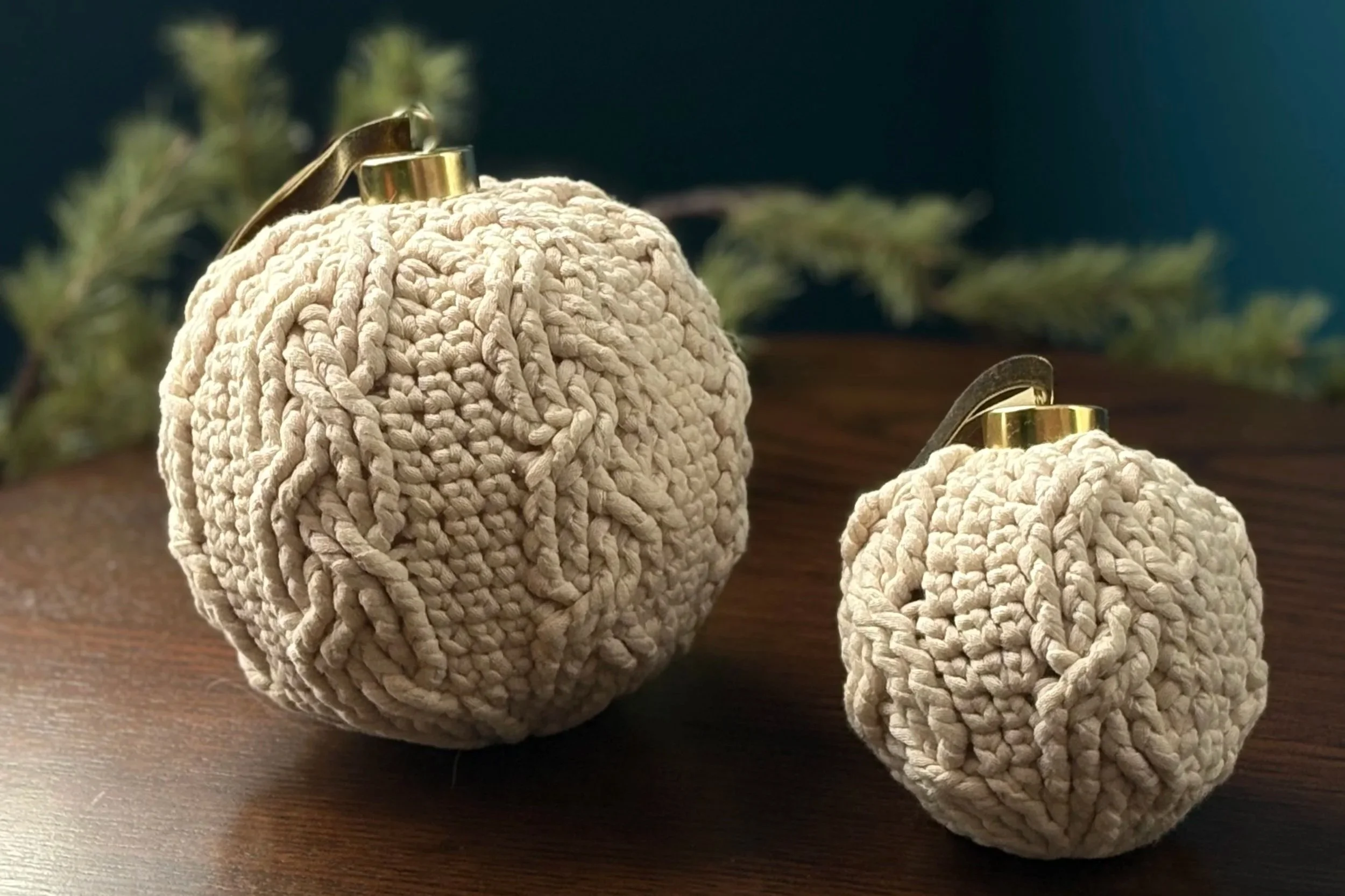 Handcrafted crocheted baubles in cream yarn with gold caps, styled on wood, showing two size variations available