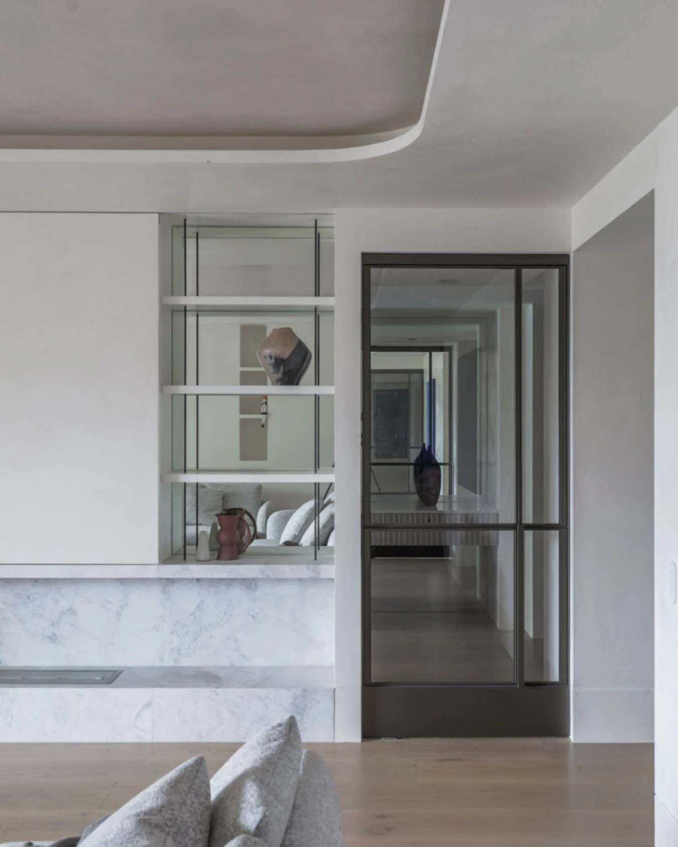 Two details that make this living room feel considered:
 
1. Mirrored backs on the open shelving &mdash; bounces light and creates depth without adding bulk.
 
2. The curved ceiling recess &mdash; adds architectural interest in a space with lower cei