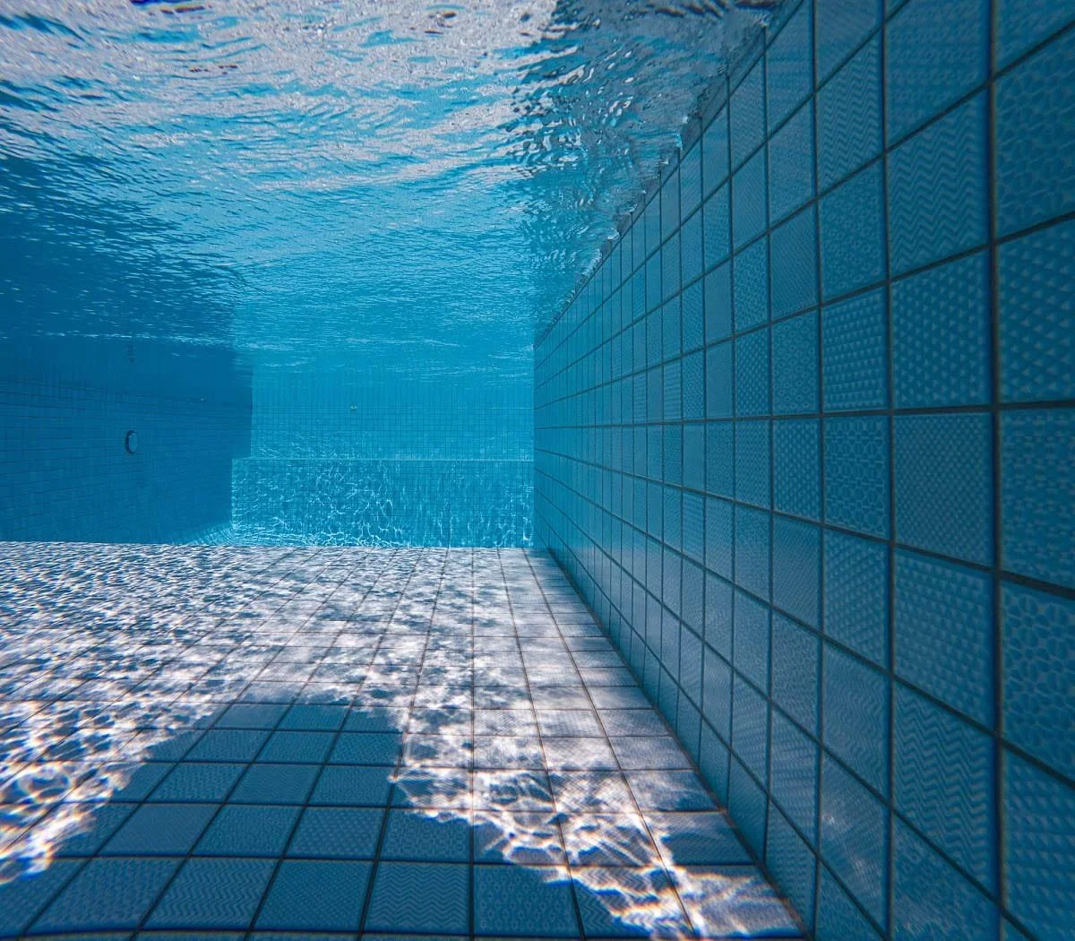 Inside view of a swimming pool with tiled walls and floor, with ripples and light reflections on the water surface.