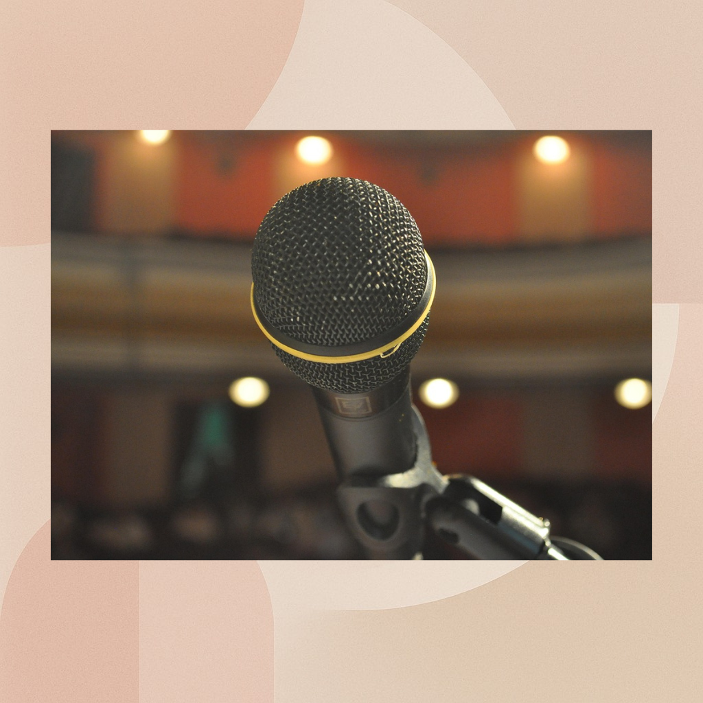 Close-up of a black microphone with a yellow ring, positioned on a stand, in a dimly lit performance venue or studio.