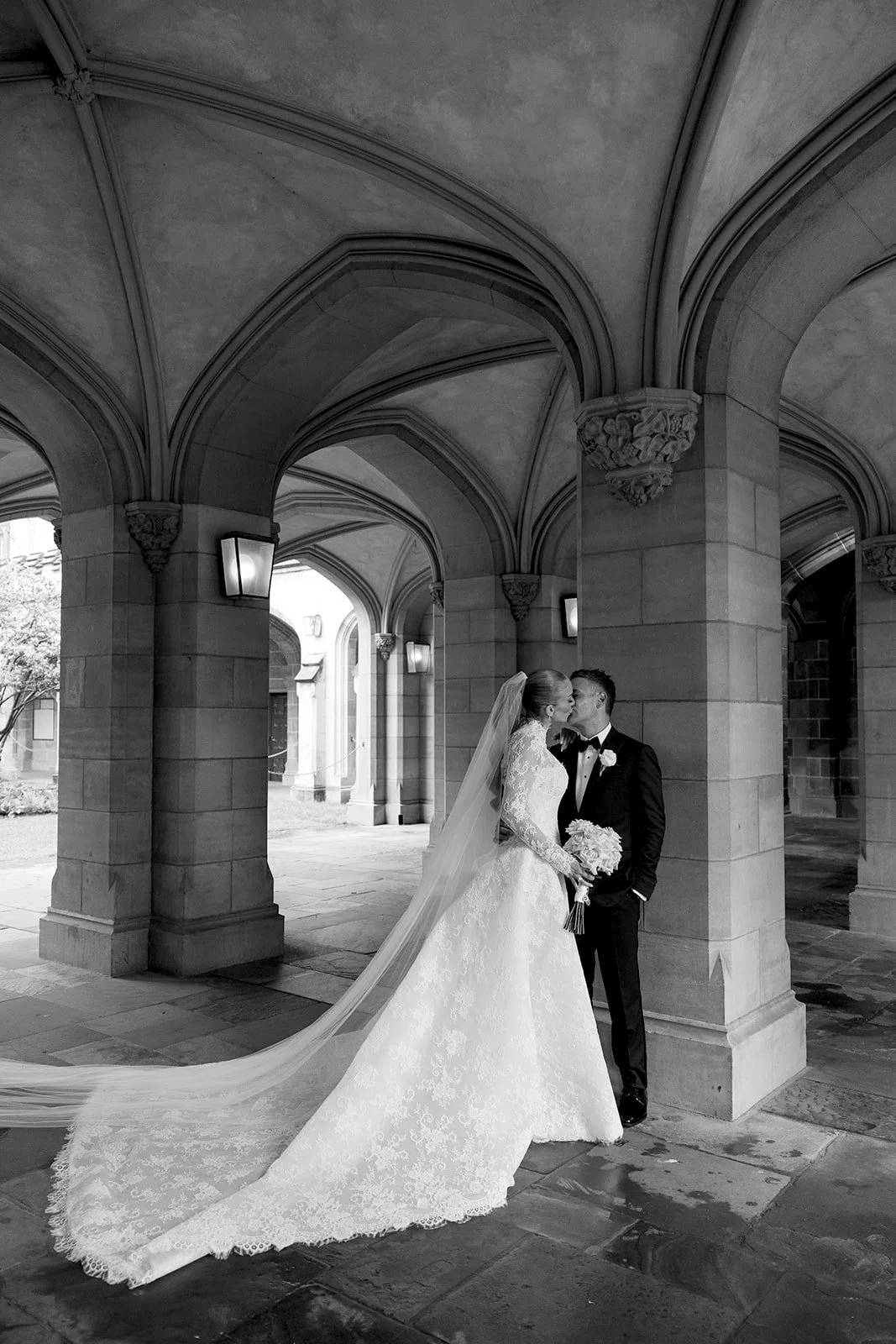 Bride and groom kissing under archways in a black and white wedding photo. Bridal Hair and Makeup by makeup artist merton muaremi