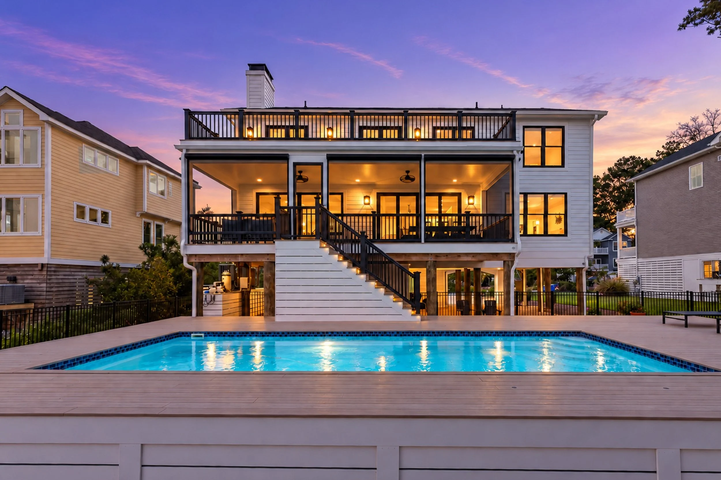 Real Estate Photography. A modern backyard with a swimming pool, wooden deck, and a two-story house with large windows and a wraparound balcony at sunset.