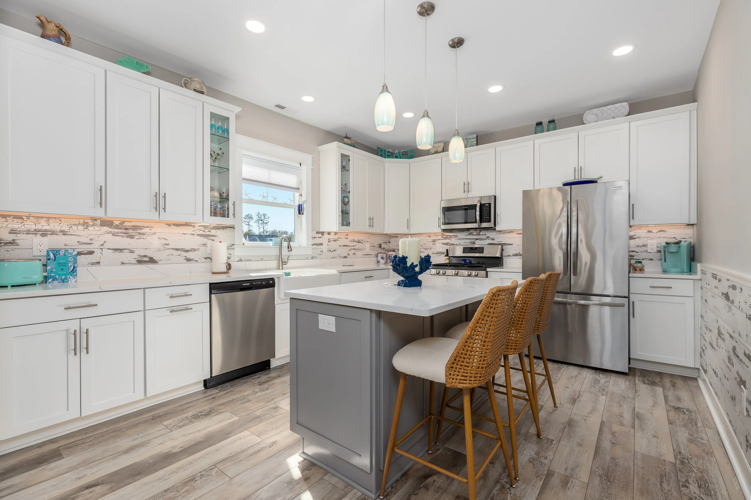 Modern kitchen with white cabinets, stainless steel appliances, a central island with seating, and wood-look flooring.