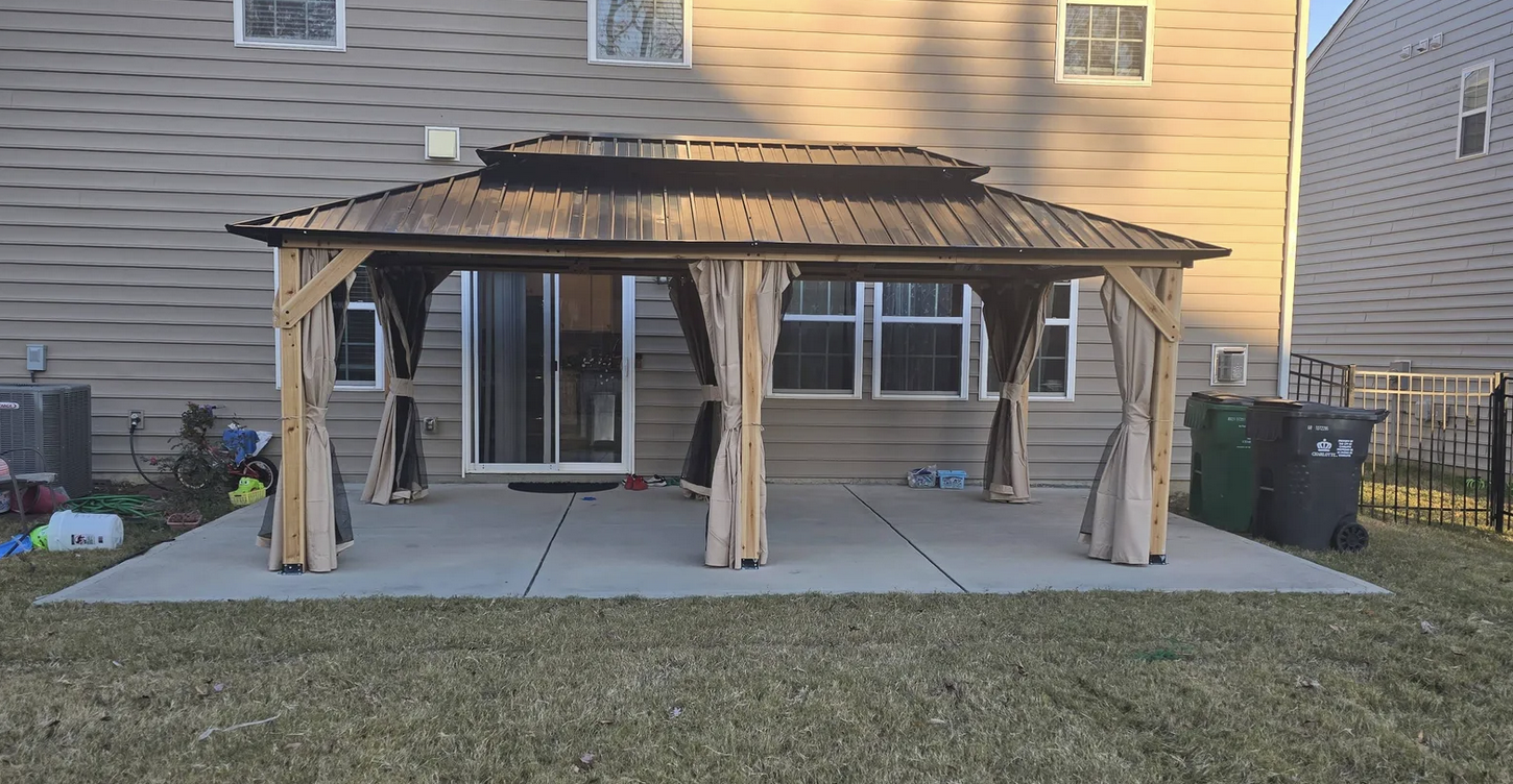 Wooden gazebo with curtains on a concrete patio in backyard