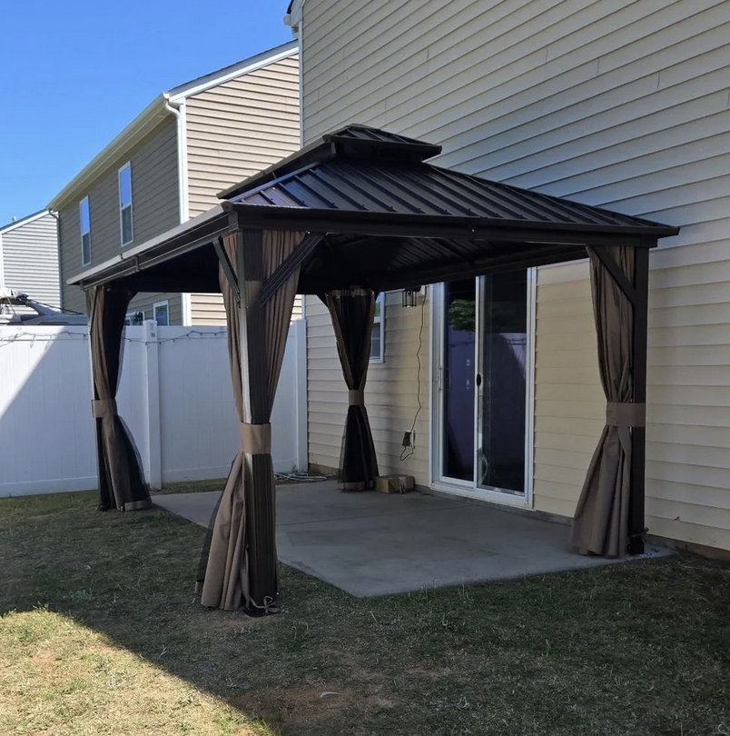 A backyard patio area with a black metal gazebo with curtains next to a beige house with a sliding glass door.