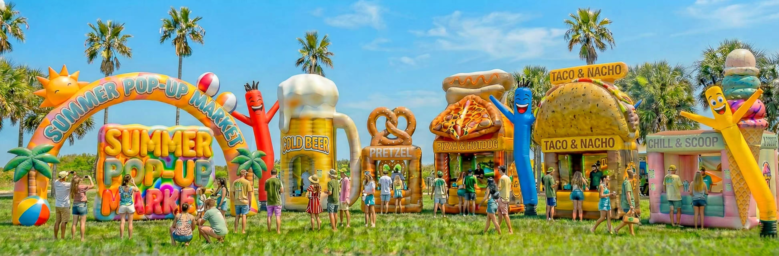 Large summer outdoor market scene featuring custom inflatable structures, including an entrance arch, inflatable beer mug booth, pizza and taco food kiosks, and air dancers for event promotion