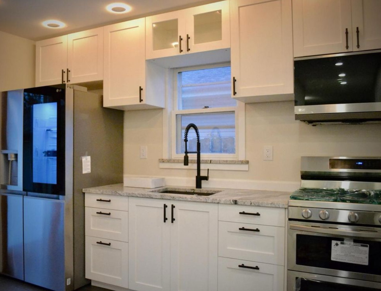 Kitchen with white cabinets, granite countertops, a black faucet, window, stainless steel refrigerator, and oven.