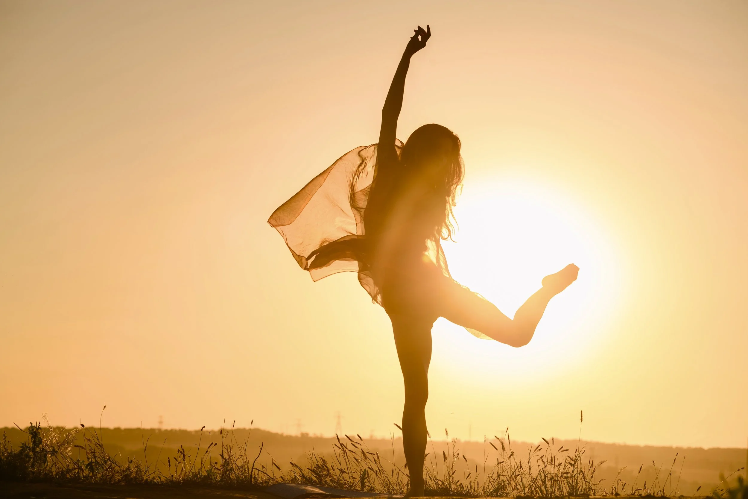 Woman practicing yoga outdoors at sunset, balancing on one leg with arms raised.