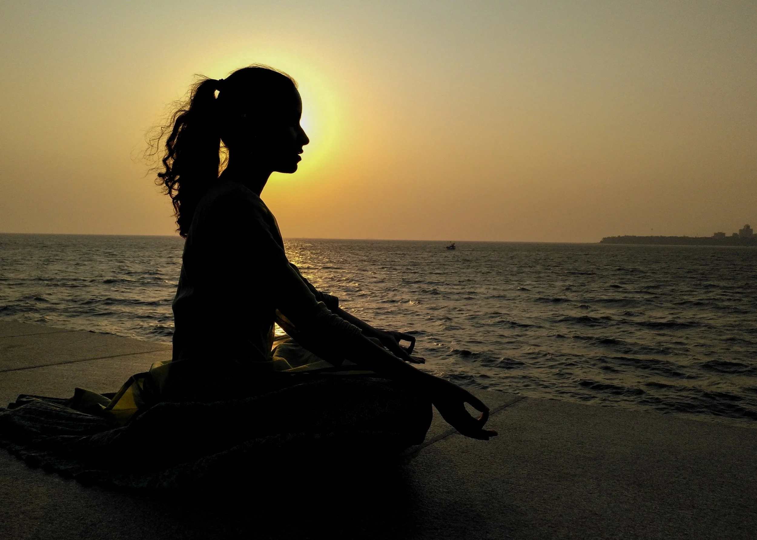 Silhouette of a woman in a meditative pose near the ocean during sunset.