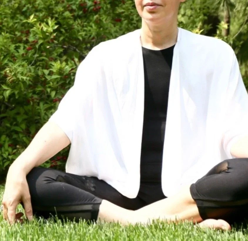 Person practicing yoga outdoors on grass, with green bushes in background. Practicing the Buddha's mudra. Touching earth at the moment of liberation.