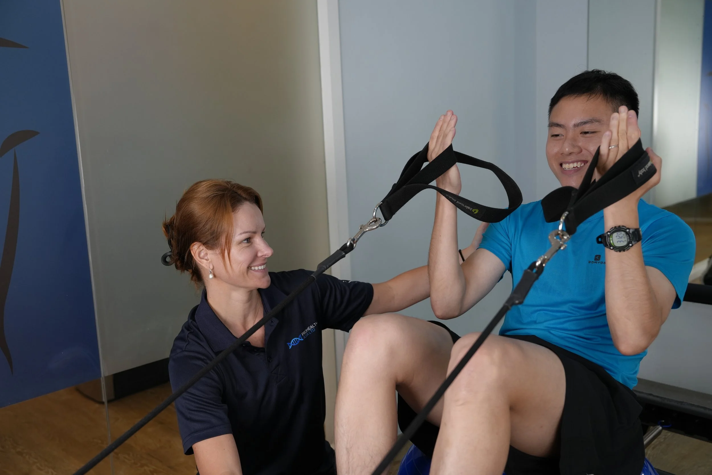 A man and a woman engaging in a physical therapy or fitness session using resistance bands, smiling and high-fiving each other.