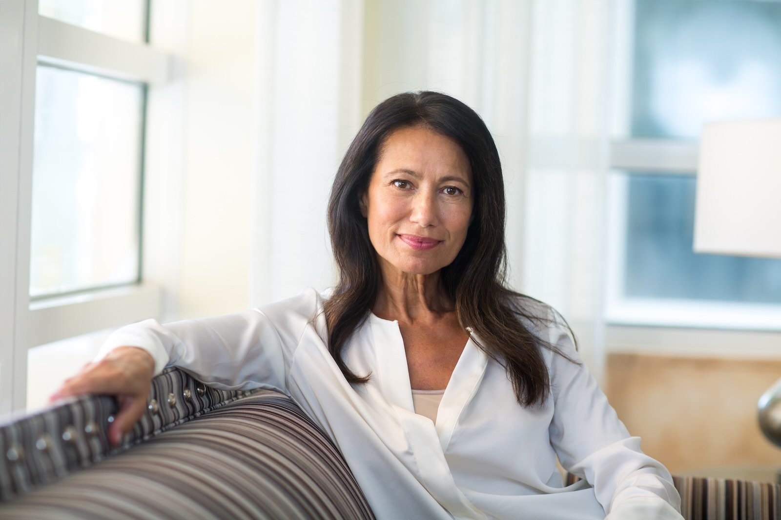 Calm, confident woman seated indoors with softly styled dark hair, reflecting a natural, polished look that feels authentic and lived-in.